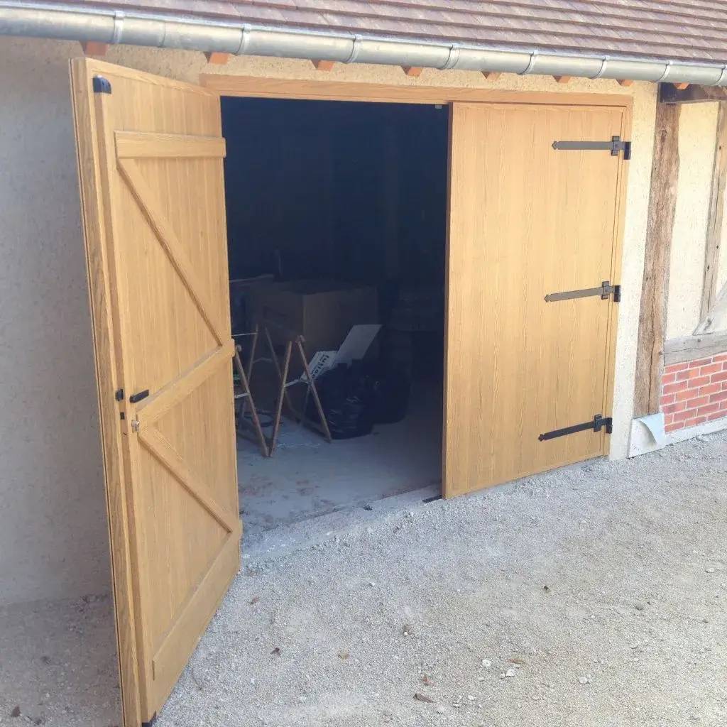 Une porte de garage en bois est ouverte, révélant un intérieur sombre avec des objets stockés à l'intérieur.