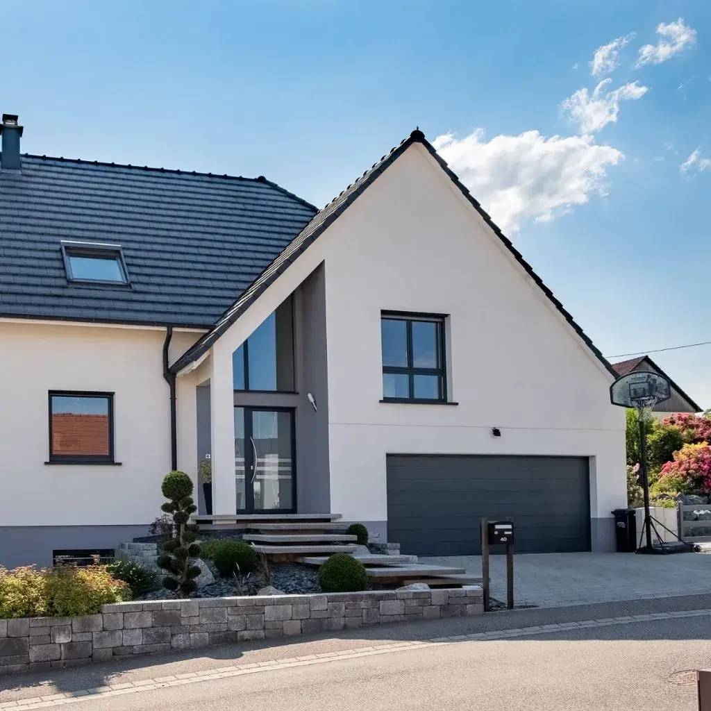 Maison contemporaine à toit incliné, avec grand garage et jardin aménagé, sous un ciel bleu clair.