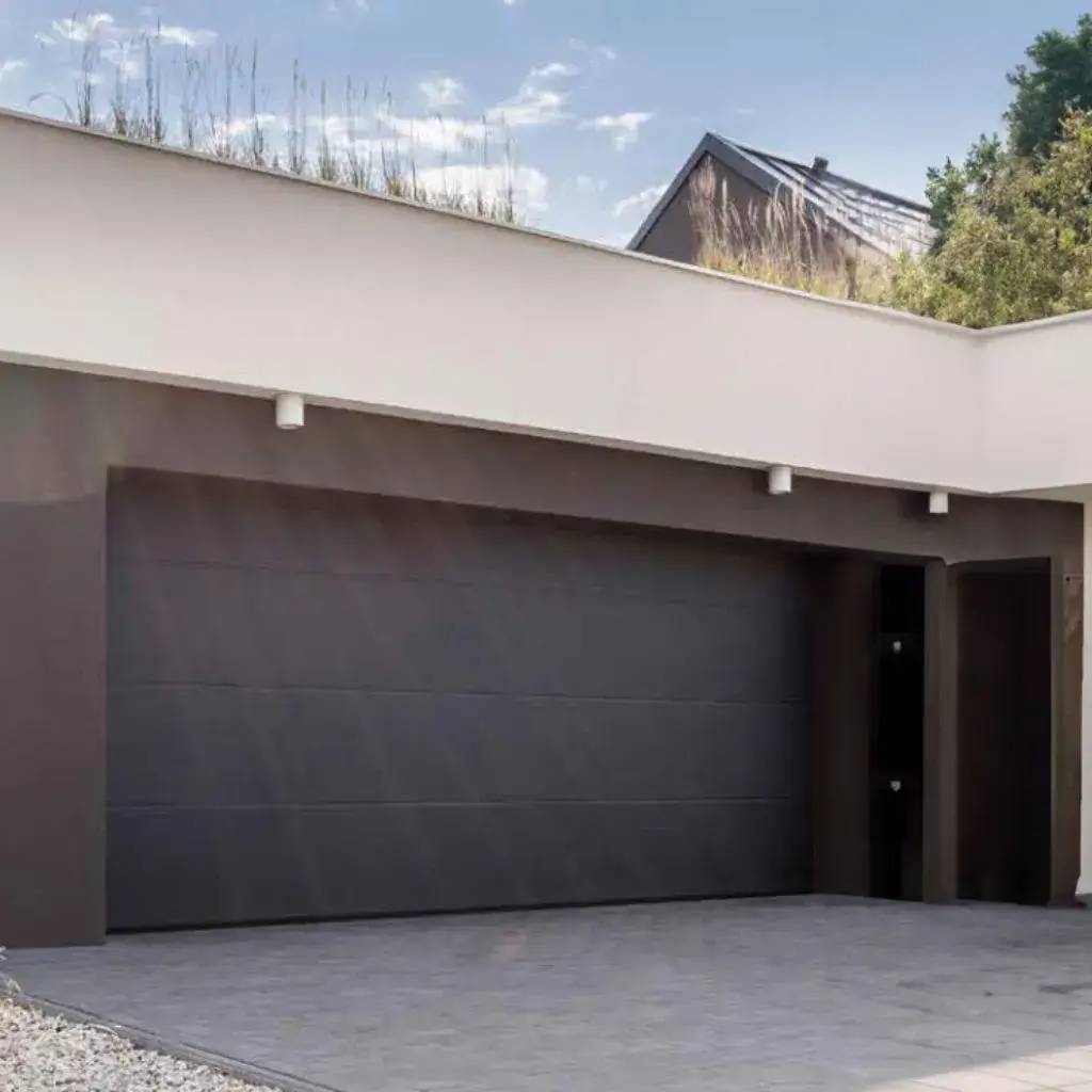 Une entrée de garage moderne avec une porte grise et un toit végétalisé sous un ciel partiellement nuageux.