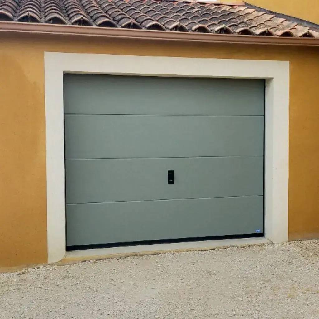 Une porte de garage sectionnelle grise intégrée dans une façade aux tons ocres.