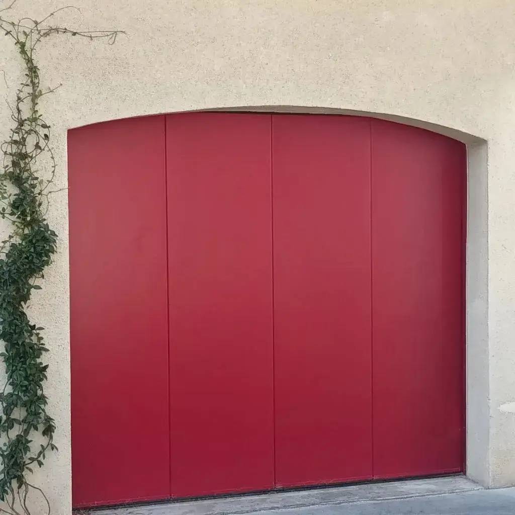 Une porte de garage rouge élégante à pans coupés, encadrée de murs beige avec un lierre grimpant sur le côté gauche.