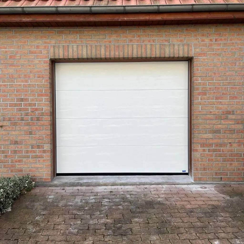 Une porte de garage blanche moderne sur une façade en briques avec un sol pavé.