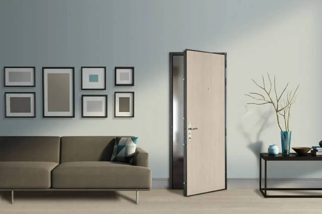 Un salon moderne avec une porte ouverte, un canapé gris, des cadres décoratifs au mur et une table avec un vase décoratif.