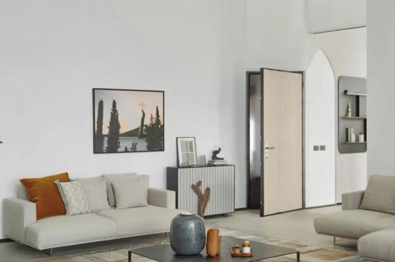 Un salon moderne et minimaliste avec un canapé beige, une table basse décorée, et un tableau sur le mur représentant un paysage forestier.