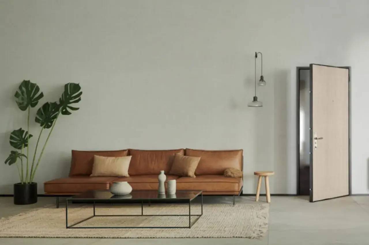 Un salon moderne et minimaliste avec un canapé en cuir marron, une table basse en verre, un tapis beige, et une plante verte.