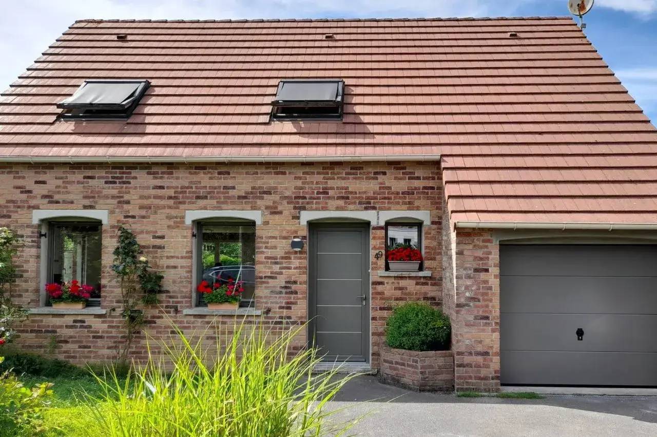 Façade en briques d'une maison avec un toit en tuiles, des fenêtres à volets noirs, des jardinières fleuries