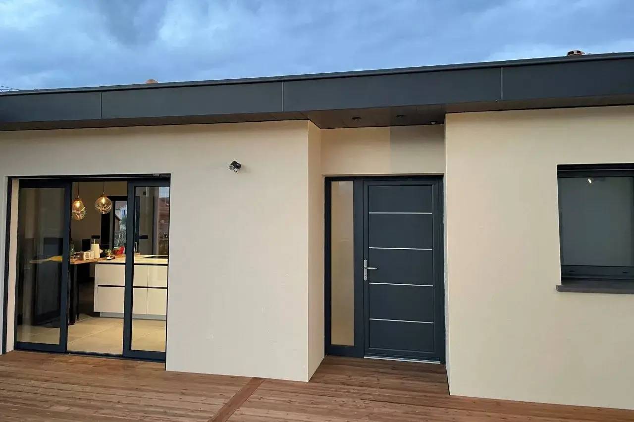 Façade moderne d'une maison avec porte et baie vitrée sur terrasse en bois.
