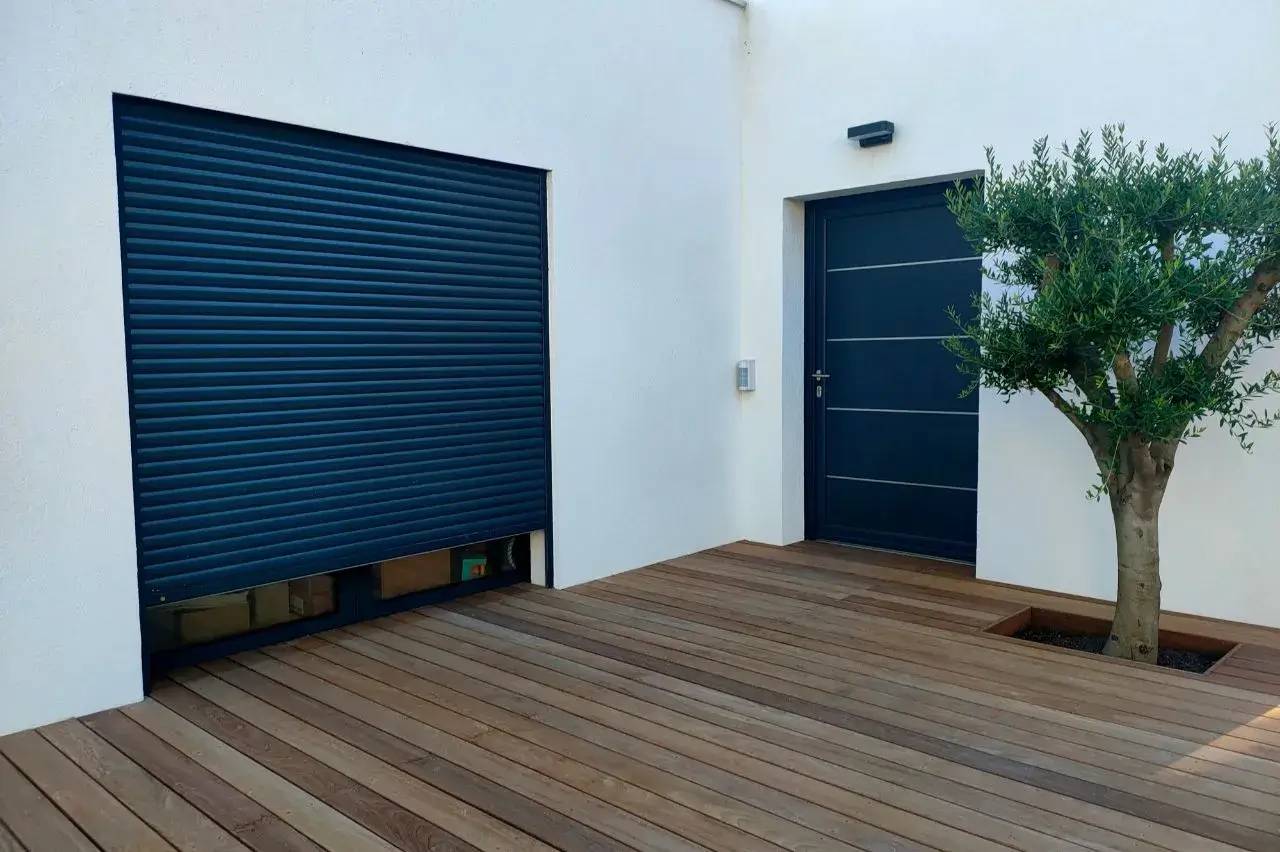 Une terrasse en bois avec une porte bleue moderne et un arbre planté dans un angle.