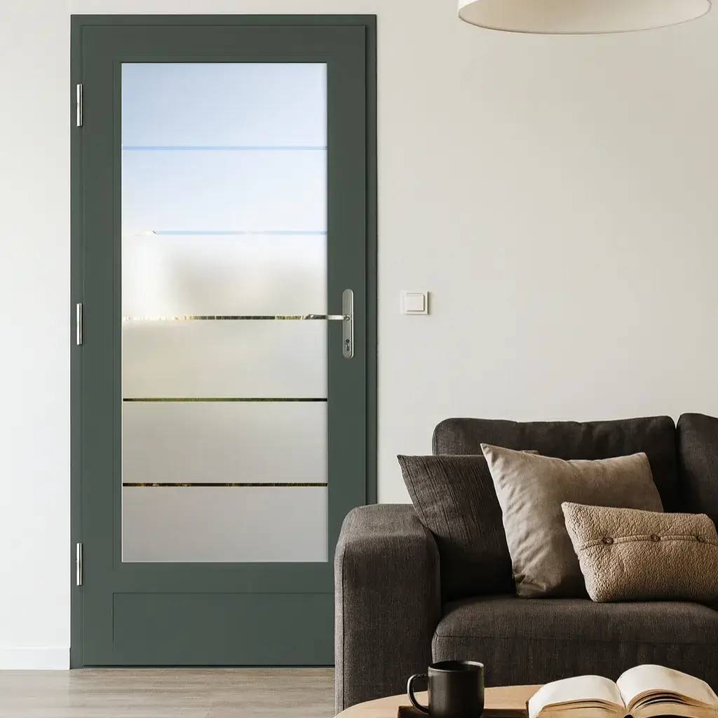 Une porte intérieure vitrée avec un cadre gris se trouve dans un salon moderne et lumineux, doté d'un canapé gris et de coussins assortis.