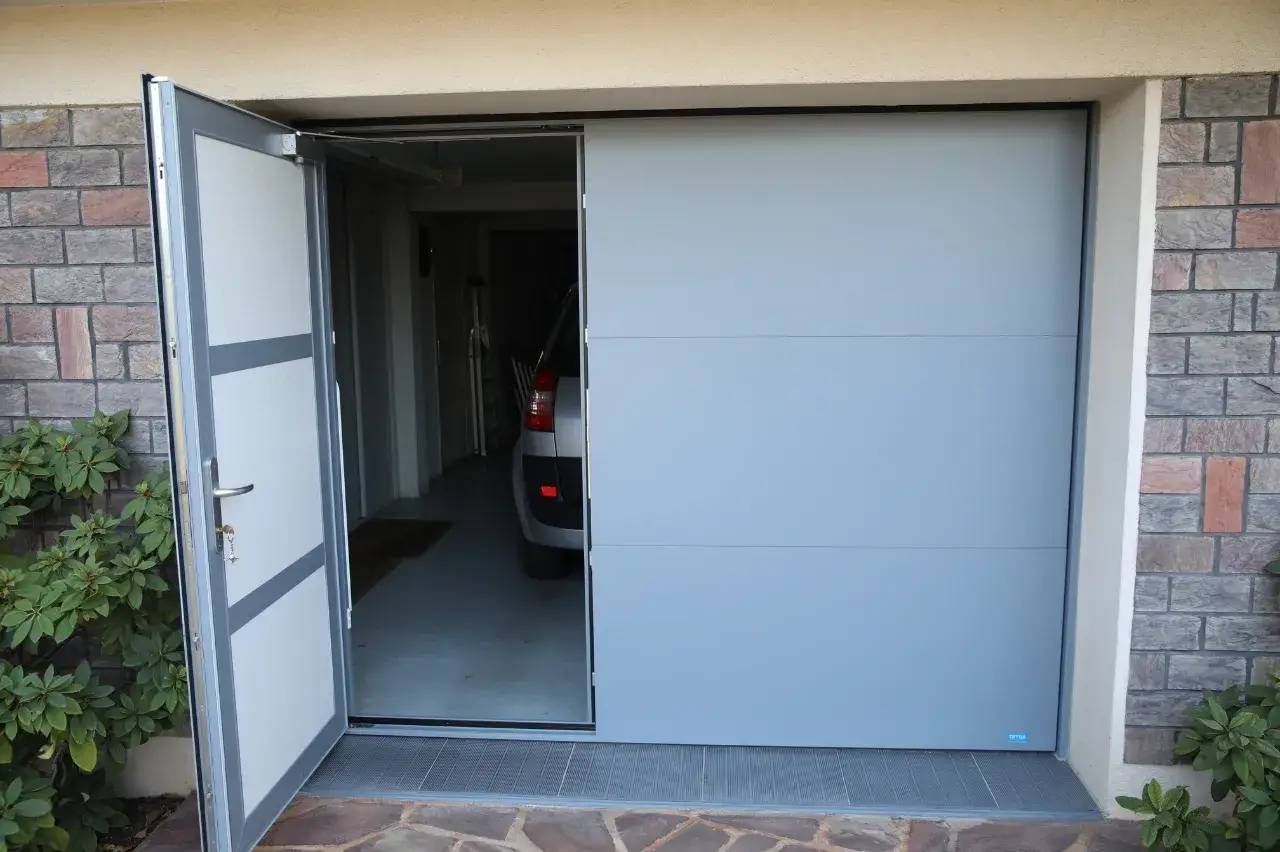 Une porte de garage moderne est partiellement ouverte, laissant entrevoir l'intérieur où est garée une voiture.