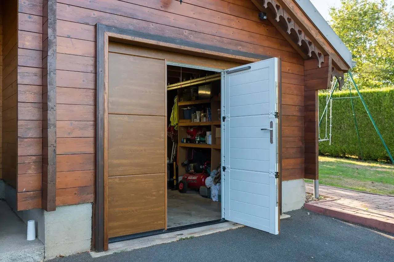 Un garage en bois avec une porte à double battant partiellement ouverte, révélant un espace de rangement organisé à l'intérieur.