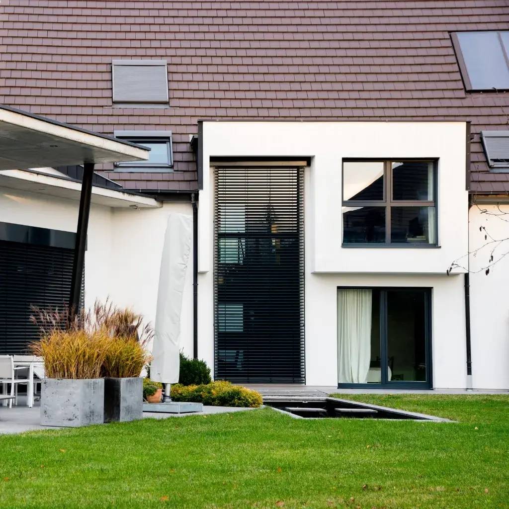 Grande maison moderne avec un jardin verdoyant, des baies vitrées et un toit en tuiles.