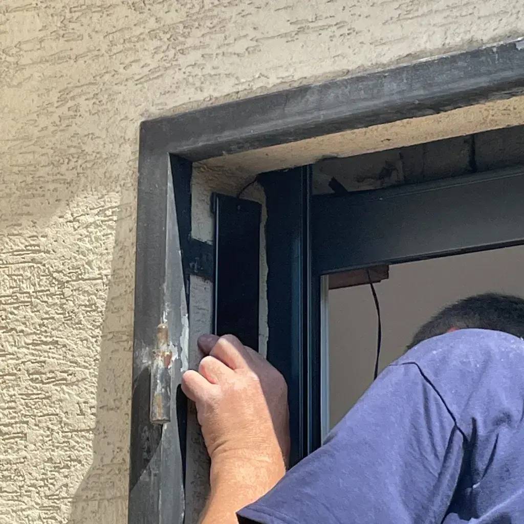 Un homme ajuste un cadre de fenêtre sur un mur extérieur texturé en plein jour.