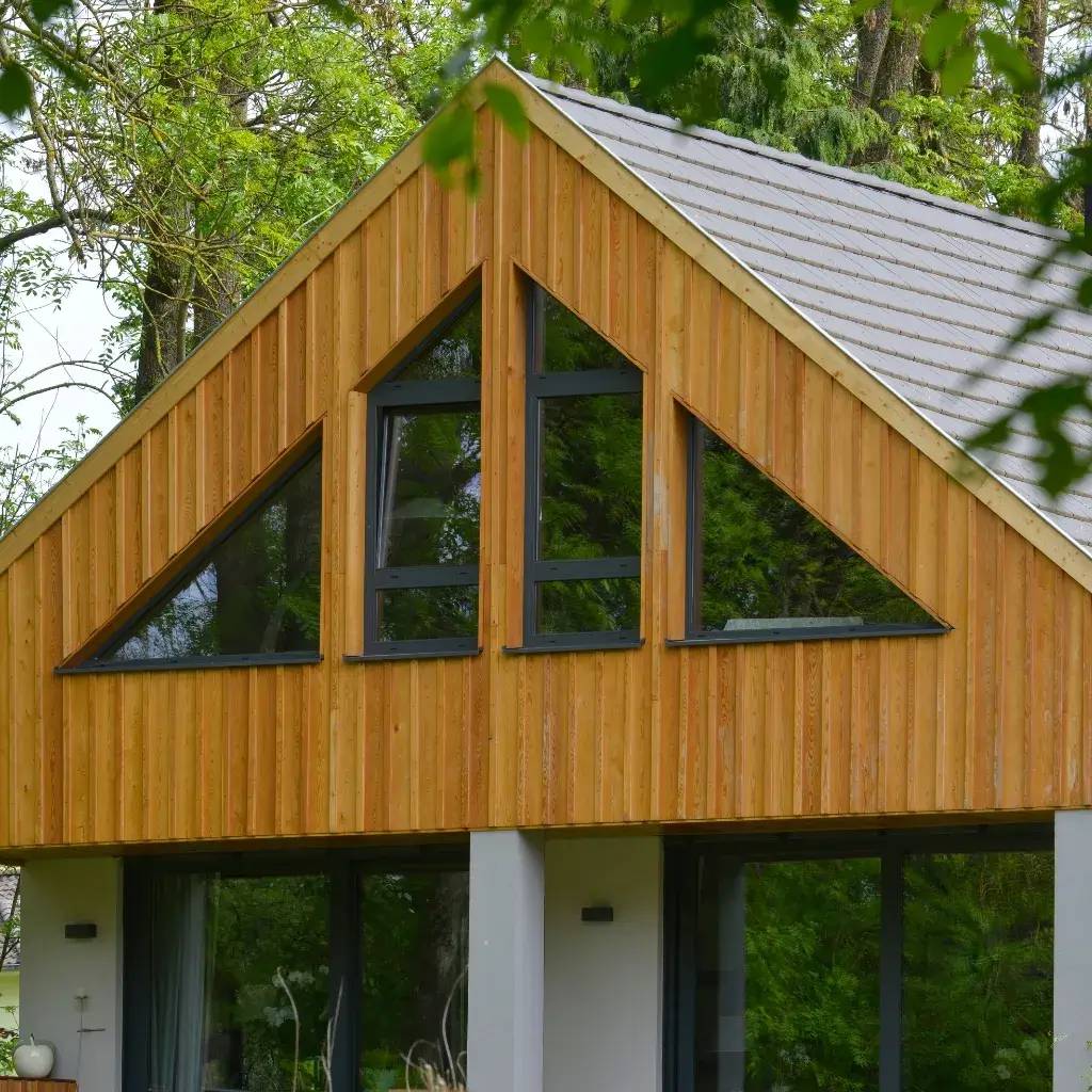 Une maison moderne avec un toit en pente et une façade en bois entourée de verdure.