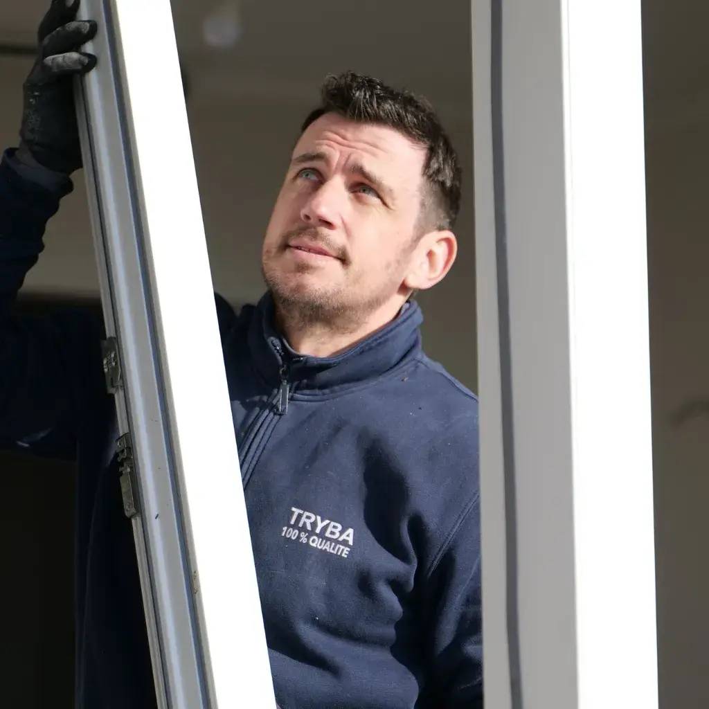 Un homme en tenue de travail inspecte ou installe une fenêtre avec concentration.