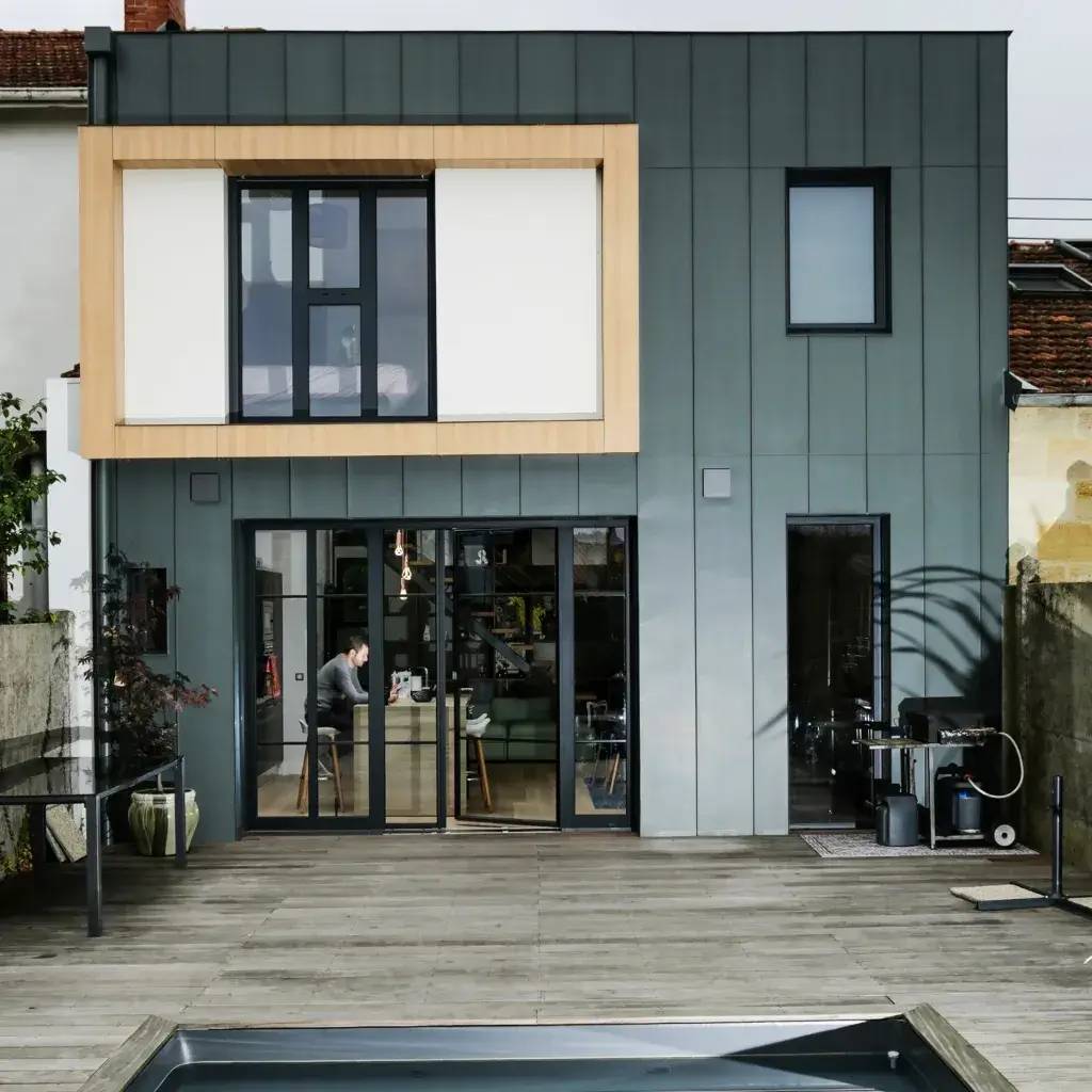 Maison moderne à deux étages avec façade en bois et métal, donnant sur une terrasse en bois avec piscine.