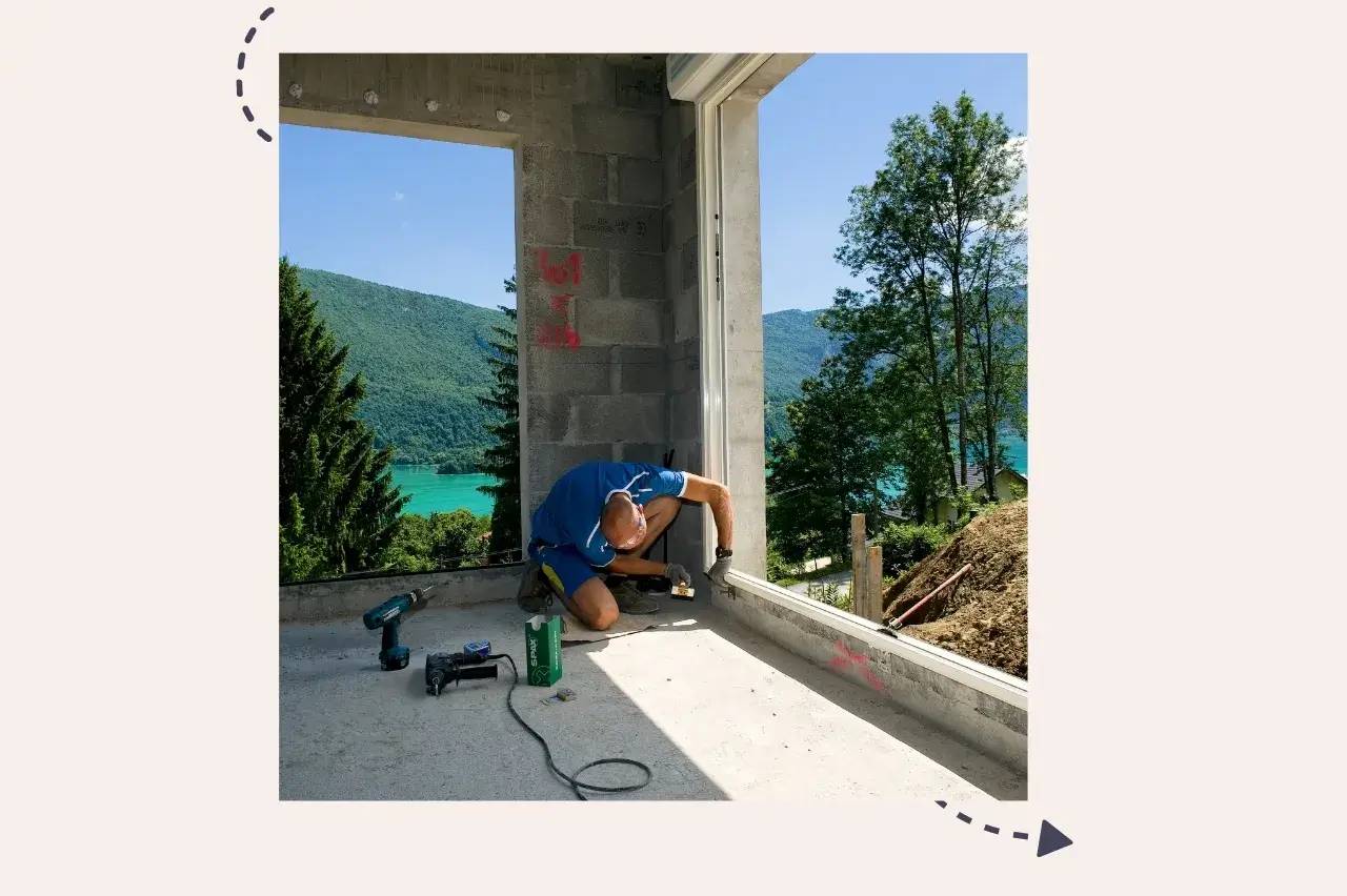 Un ouvrier travaille sur un chantier de construction avec vue sur un paysage de lac et montagne.