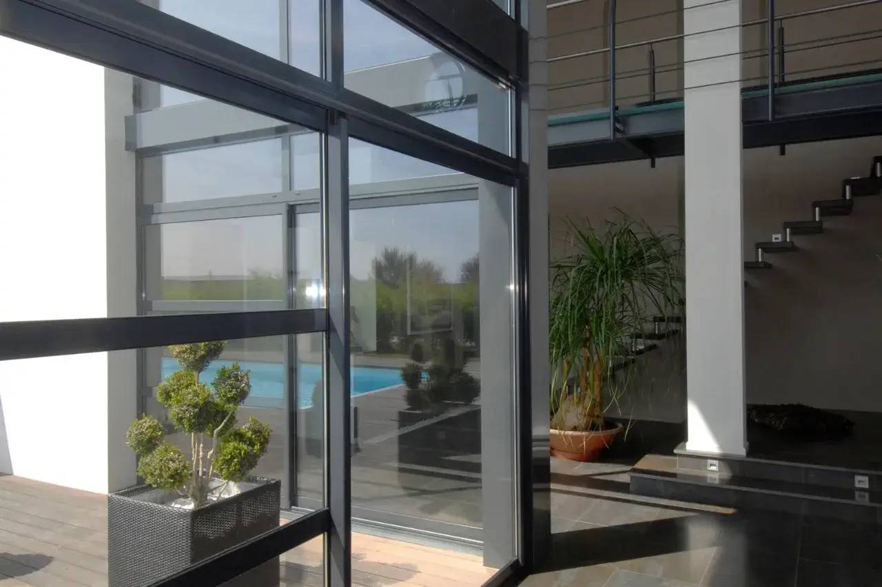 Cette image montre un intérieur moderne et lumineux avec de grandes baies vitrées, des plantes d'intérieur et un escalier menant à un étage supérieur