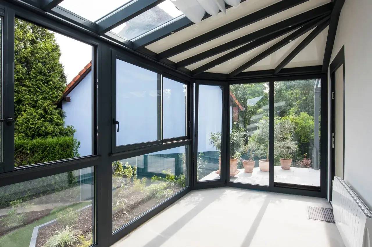 Une lumineuse véranda contemporaine avec de grandes baies vitrées donnant sur un jardin verdoyant.