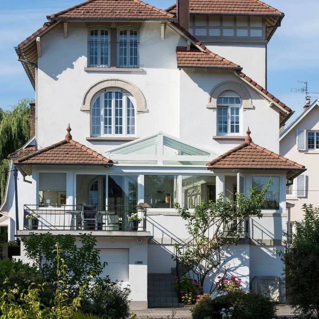 Une maison élégante à l'architecture classique avec un toit en tuiles brunes, des fenêtres arquées et une véranda lumineuse entour
