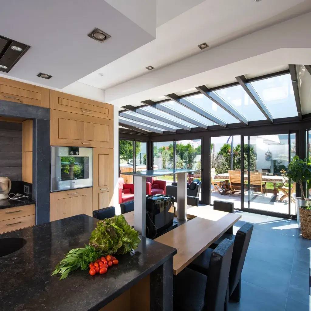 Une cuisine moderne et lumineuse avec un îlot central, s'ouvrant sur une terrasse ensoleillée grâce à de grandes baies vitrées