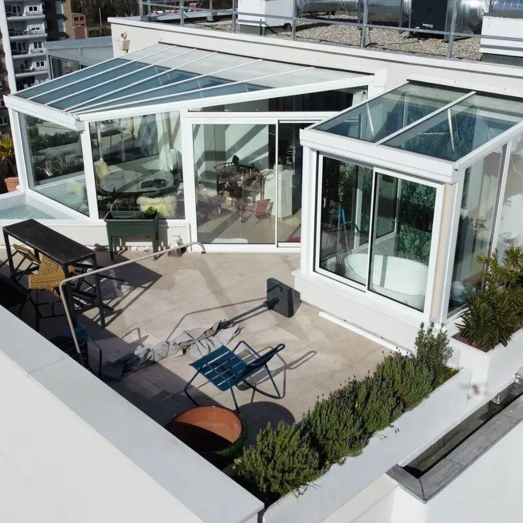 Cette image montre une terrasse moderne sur un toit avec une véranda en verre et un espace détente.