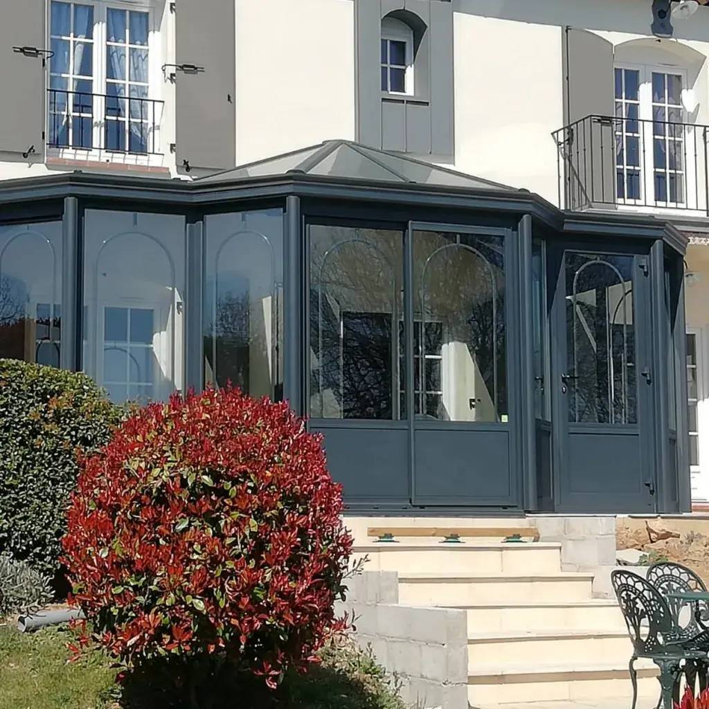 Cette image montre une véranda moderne en verre et métal sombre, entourée d'un jardin paysager.