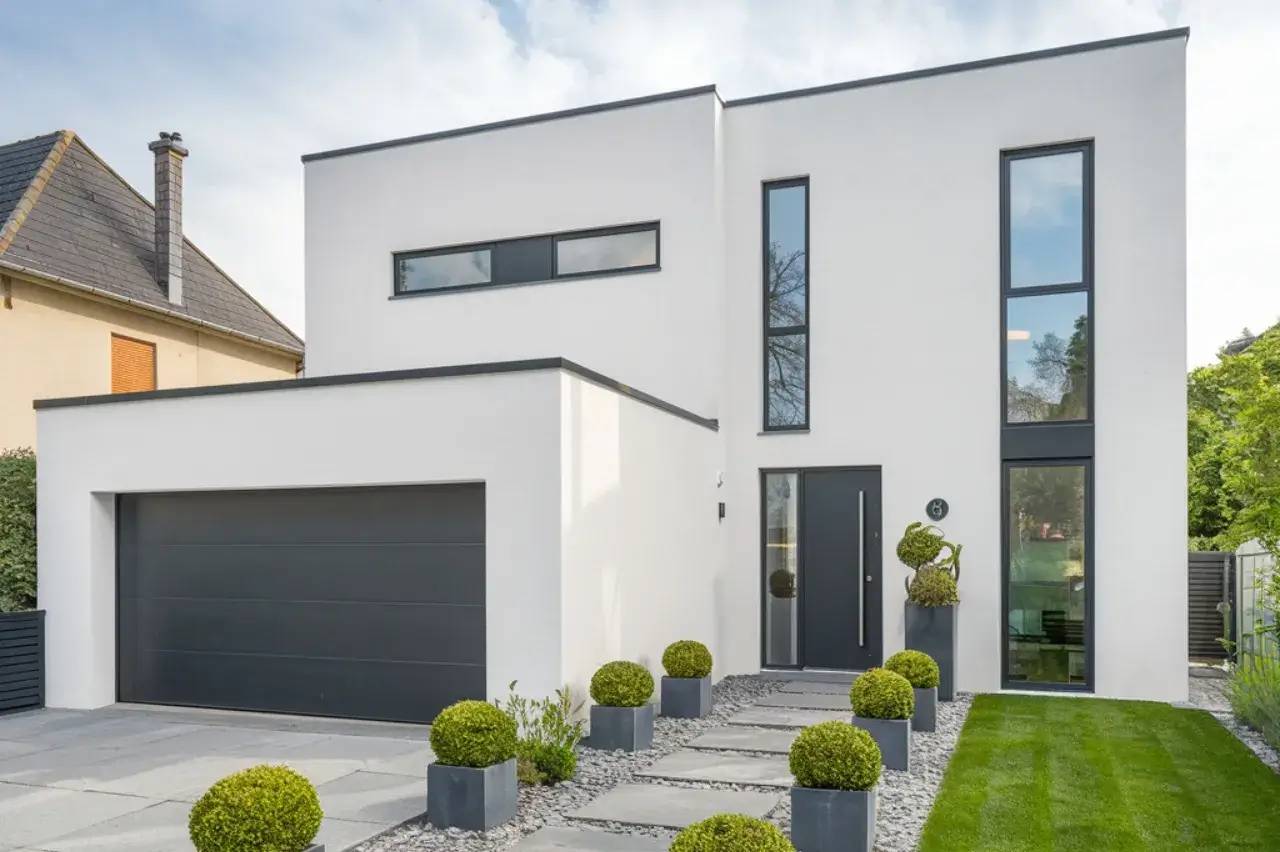 Maison contemporaine au design épuré, avec façade blanche, grandes fenêtres et jardin soigné bordé de buis taillés.