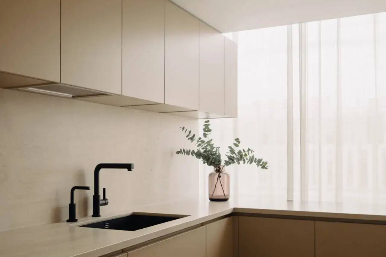 Une cuisine moderne et épurée avec un robinet noir au-dessus d'un évier intégré et un vase transparent avec des feuillages sur le plan