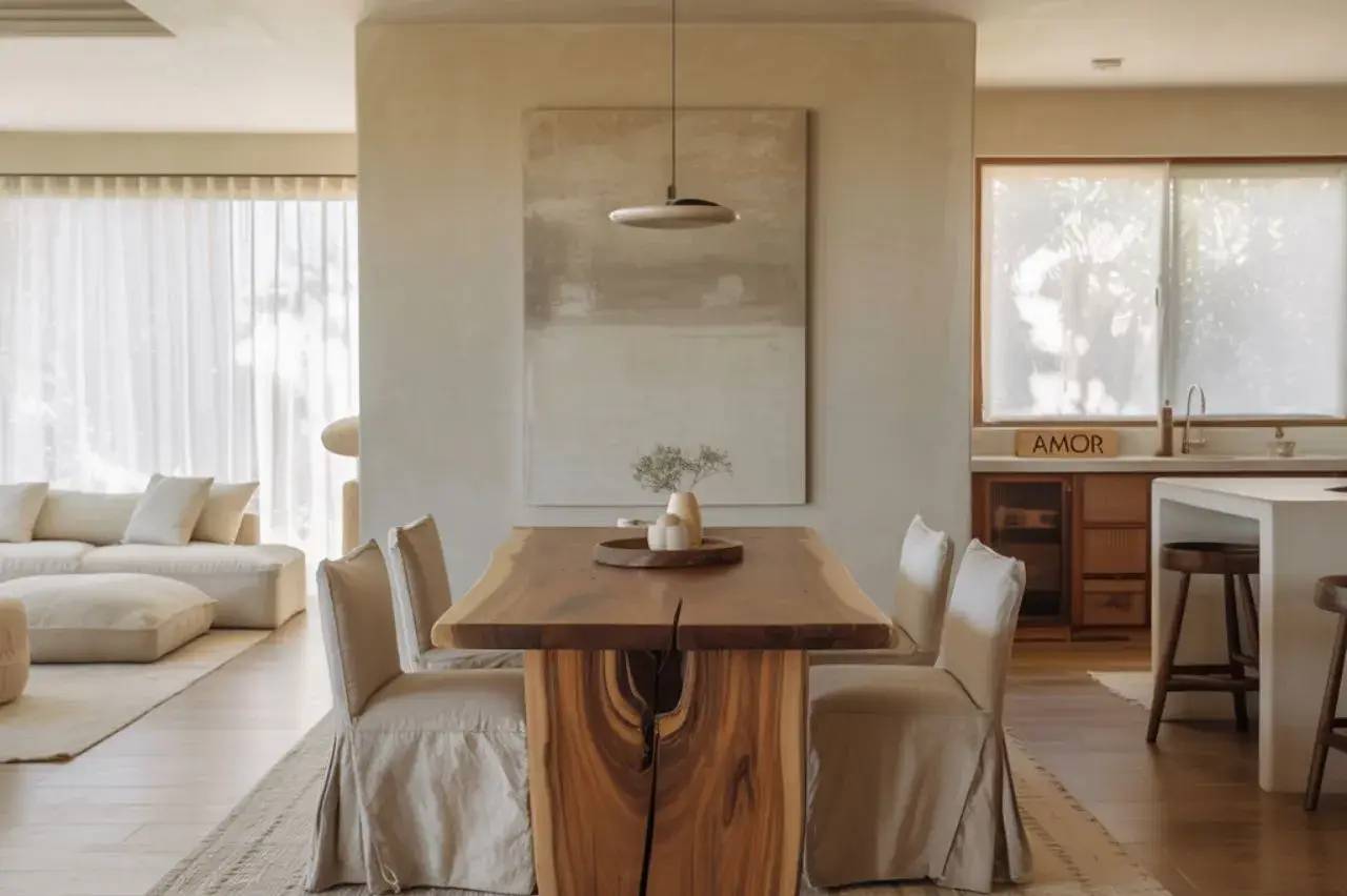 Salle à manger moderne avec une table en bois massif, entourée de chaises en tissu beige, dans un espace lumineux et épuré.