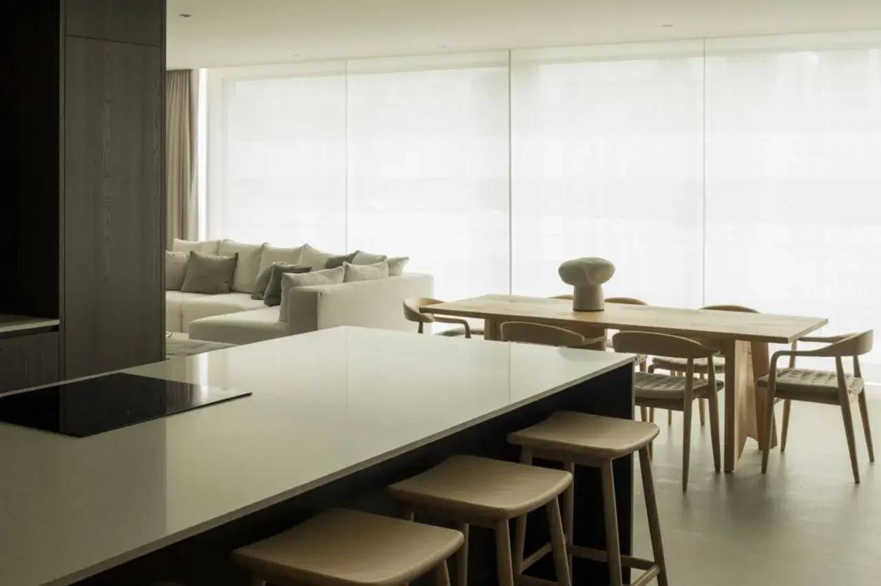 Un intérieur moderne et lumineux avec une cuisine ouverte sur un salon et salle à manger minimalistes, dotés de meubles en bois clair et de grandes fenêtres