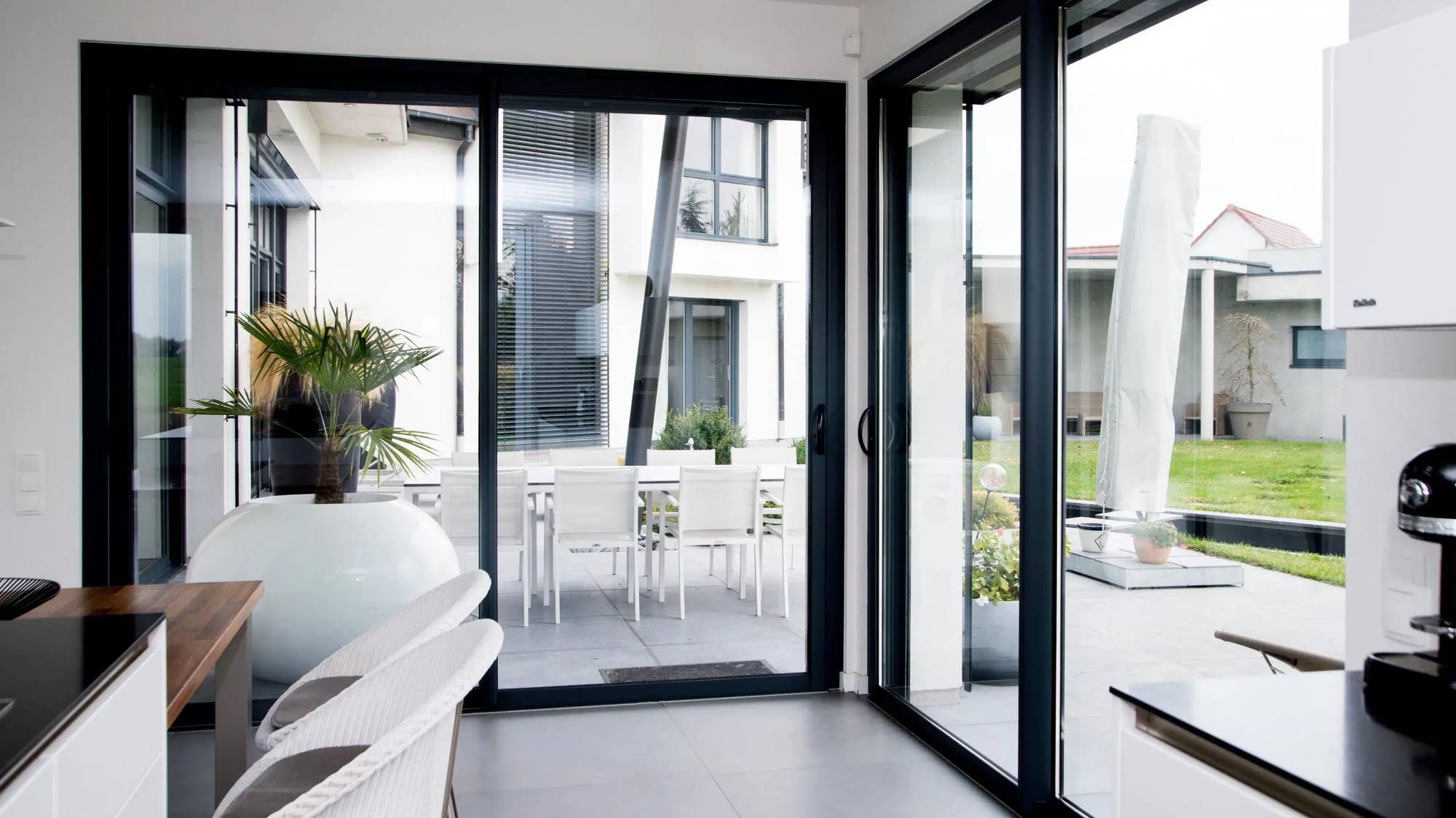 Une cuisine moderne lumineuse avec de grandes baies vitrées offrant une vue sur un jardin et une terrasse élégante.