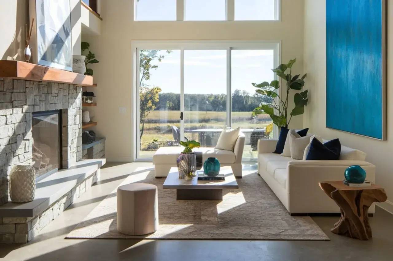 Un salon moderne et lumineux avec un mobilier épuré, un grand tableau bleu, une cheminée en pierre et une vue dégagée sur l'extérieur grâce aux