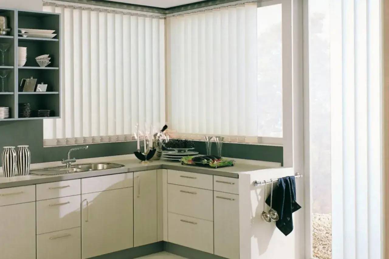 La cuisine moderne est lumineuse et équipée de placards blancs avec des stores verticaux laissant entrer la lumière naturelle.