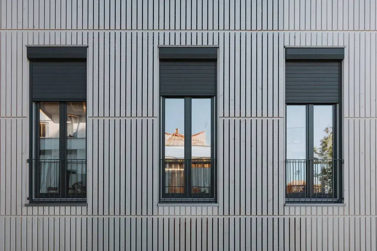 Façade moderne avec trois fenêtres alignées sur un revêtement extérieur à rayures verticales grises.