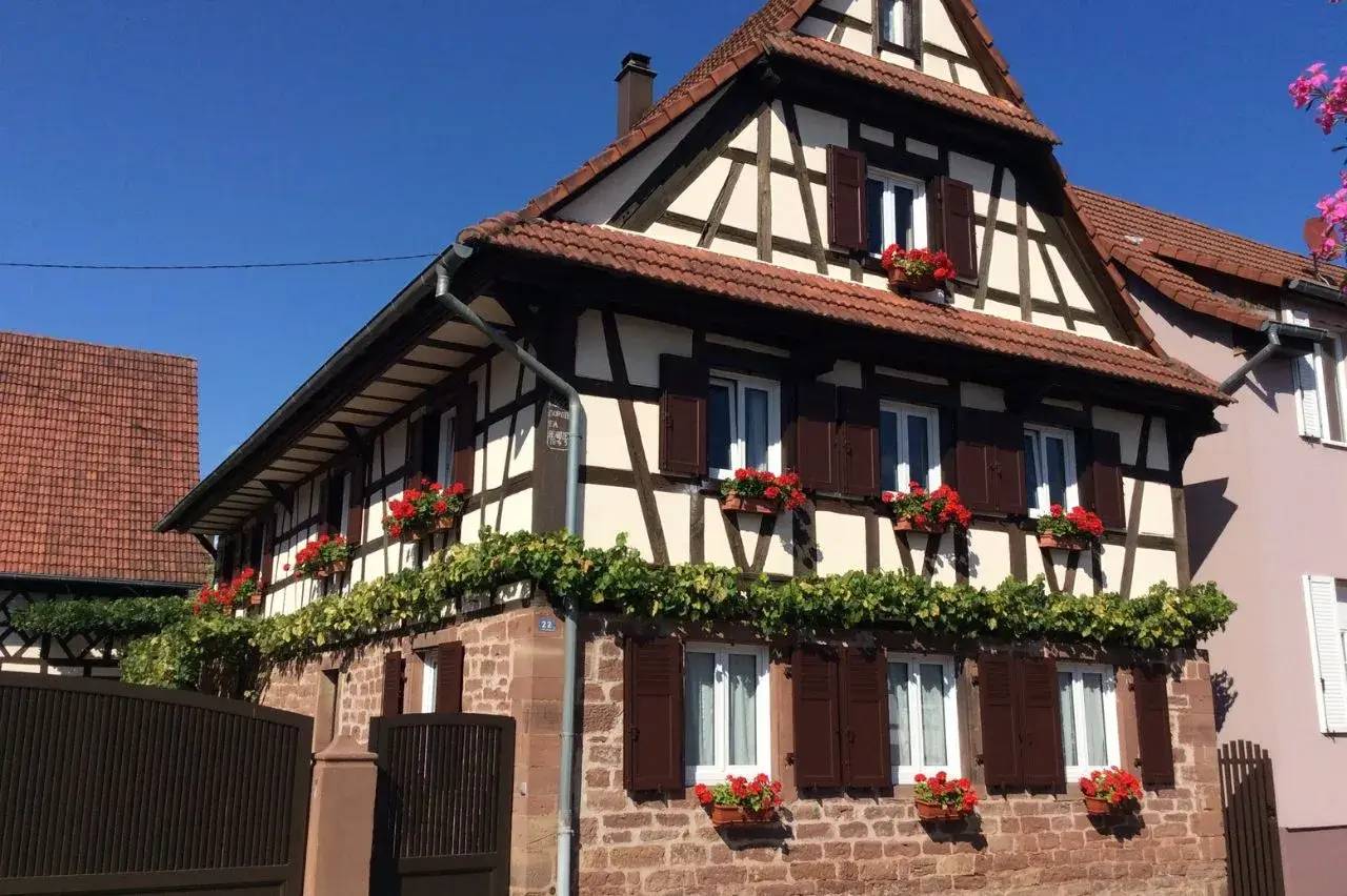 Maison à colombages traditionnelle avec des fleurs rouges aux fenêtres, située sous un ciel bleu clair.