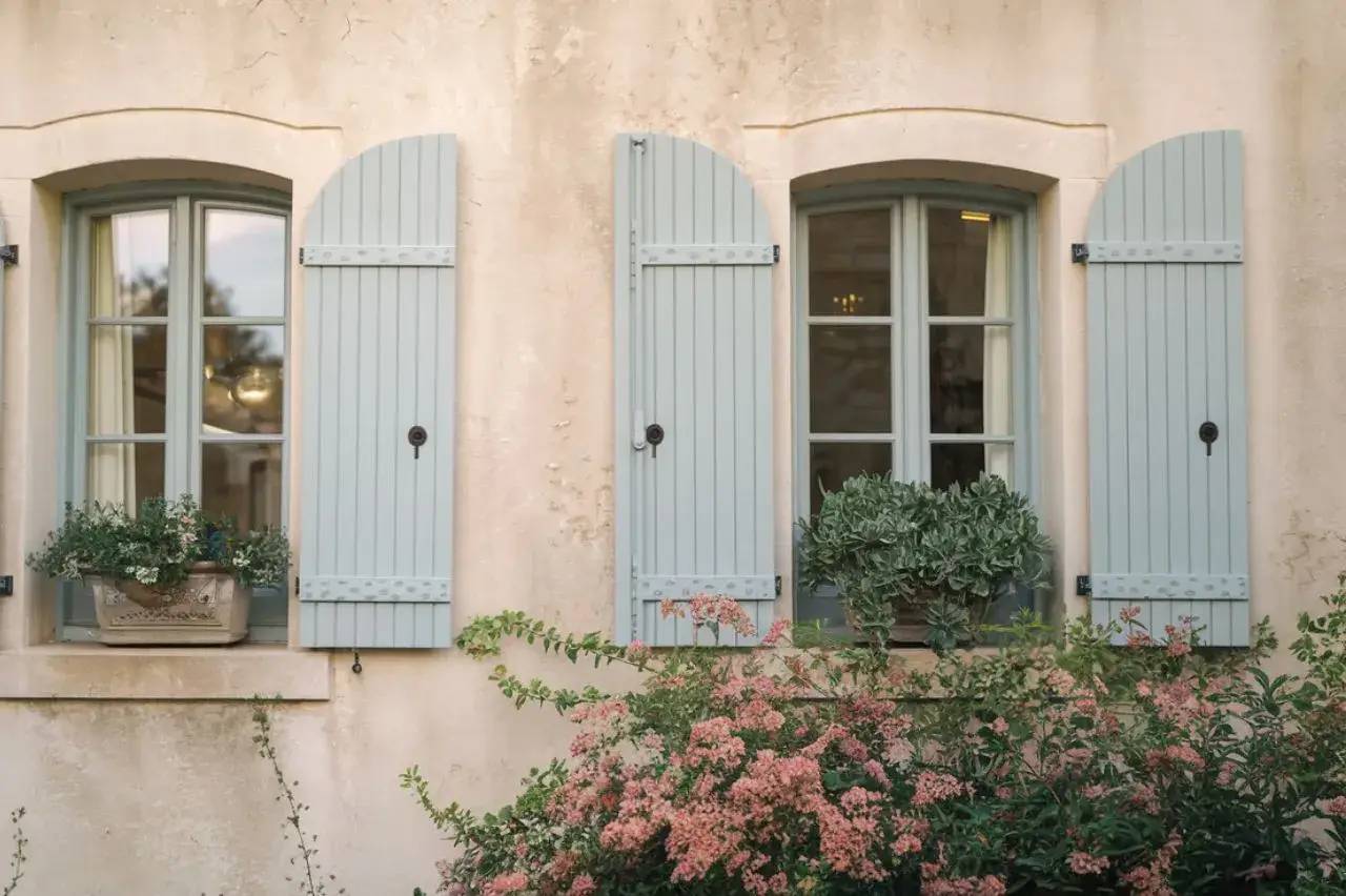 Façade de maison provençale avec des volets bleus et des plantes fleuries en avant-plan.