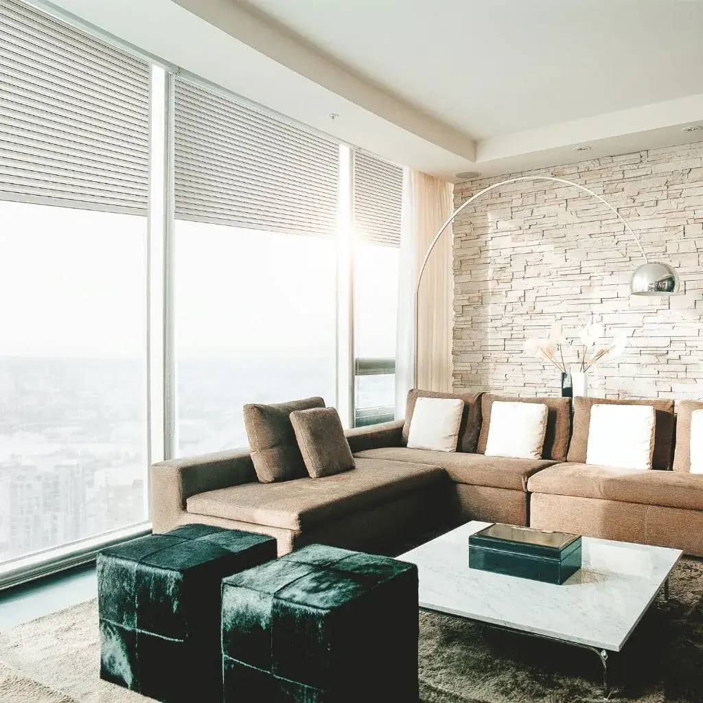 Un salon moderne et élégant avec un canapé d'angle marron, des poufs noirs, une table basse en marbre et un mur en pierre