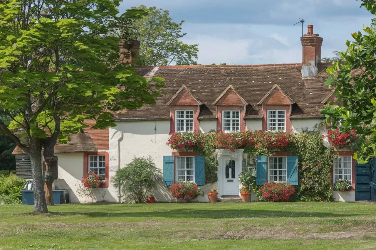 Une charmante maison de campagne avec des volets bleus et des fleurs colorées ornant la façade.