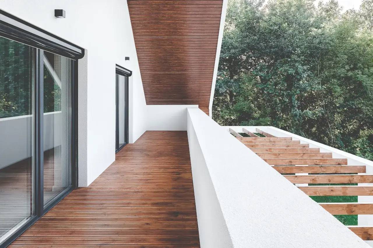 Une terrasse moderne en bois avec garde-corps blancs, surplombant une forêt luxuriante.