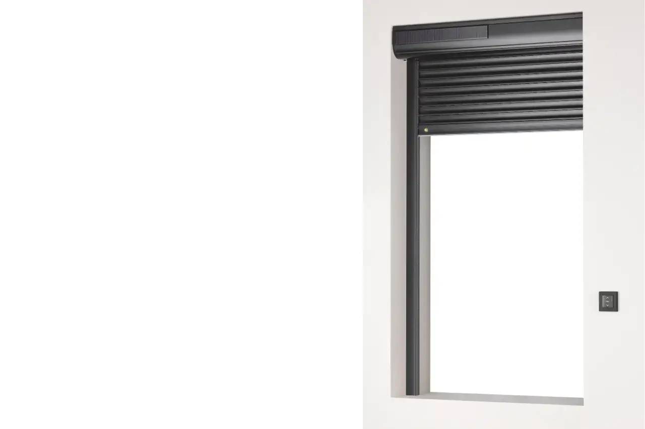 Volet roulant gris foncé partiellement ouvert sur une fenêtre encastrée dans un mur blanc.