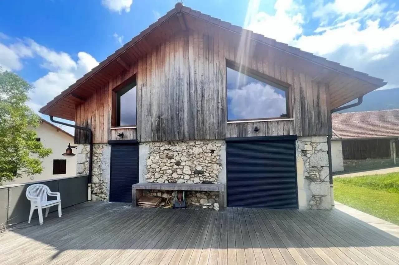 Une maison en bois au design rustique avec un toit à deux pentes et de grandes fenêtres reflétant un ciel bleu.