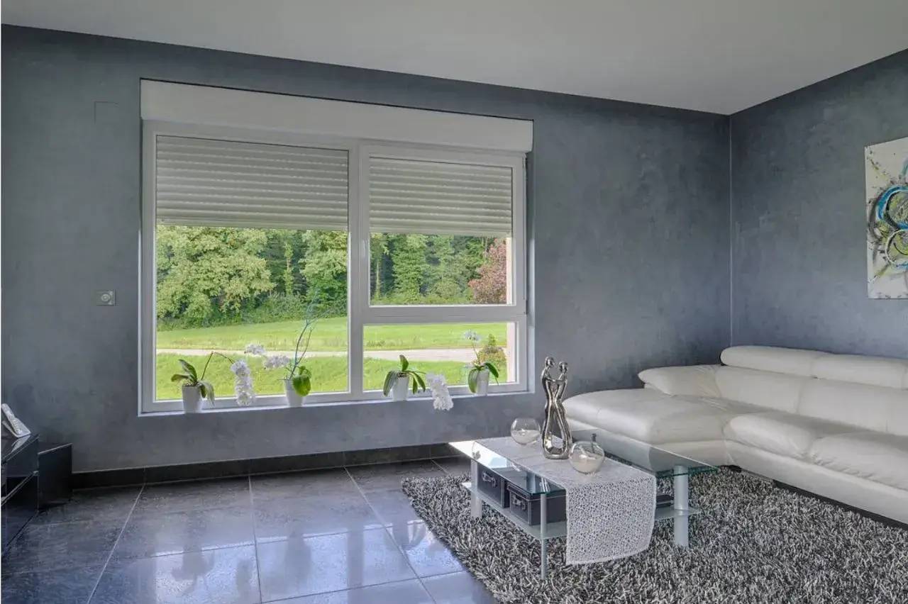 Un salon moderne et élégant avec un canapé blanc, une table basse en verre et une grande fenêtre donnant sur un espace verdoyant.