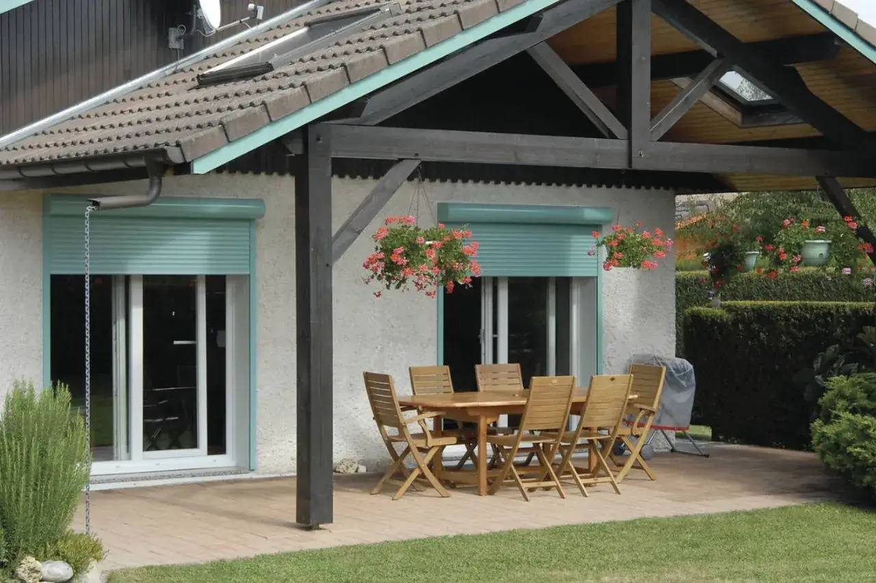 Une terrasse en bois couverte avec une table à dîner et des chaises, entourée de plantes et de fleurs suspendues.
