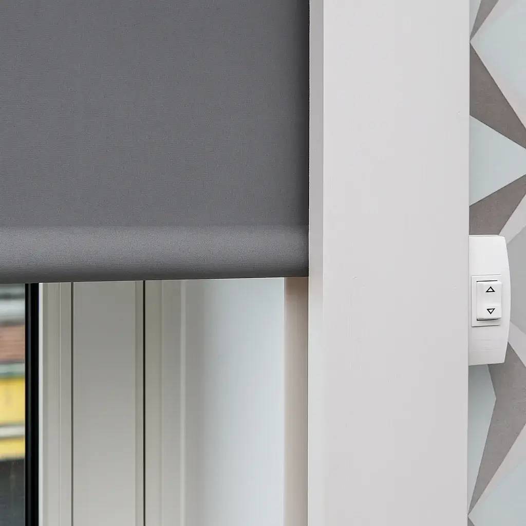 Une fenêtre avec un store gris électrique et un interrupteur mural intégré.