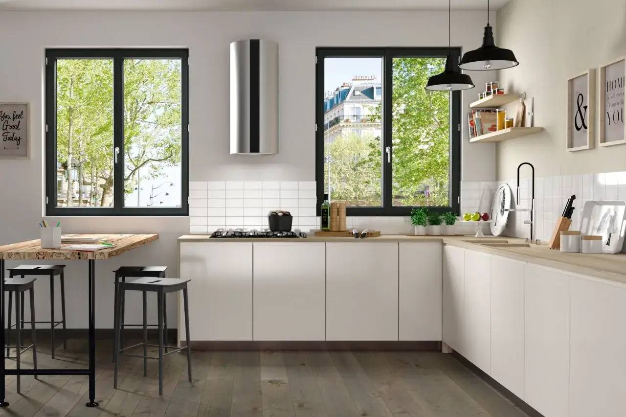 Cuisine moderne et lumineuse avec un mobilier blanc minimaliste, de grandes fenêtres donnant sur des arbres verts, et un espace de cuisson équipé.