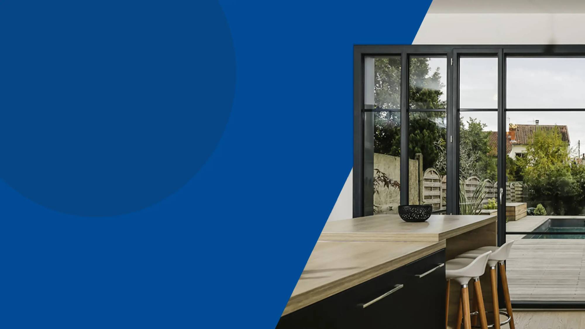 Une cuisine moderne avec un îlot et de grandes fenêtres s'ouvrant sur une terrasse en bois et une piscine.