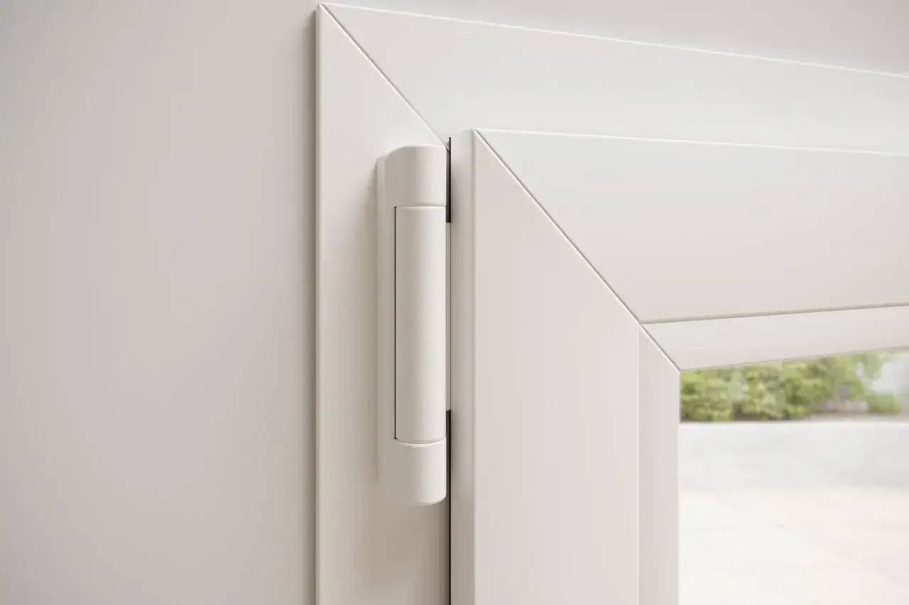 Détail d'une charnière discrète sur une fenêtre en PVC blanc.