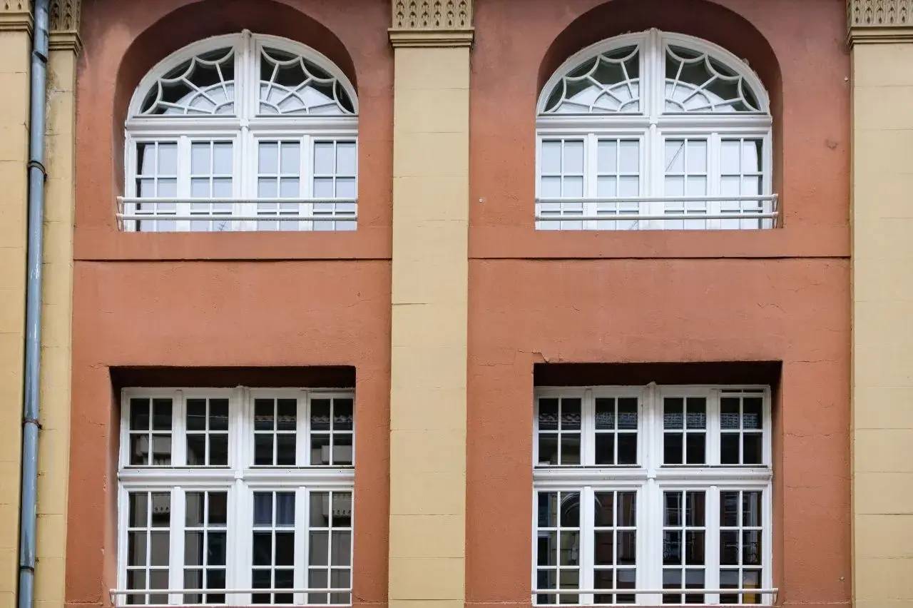 Façade en brique rouge avec fenêtres blanches à arc légèrement voûté et motifs géométriques.