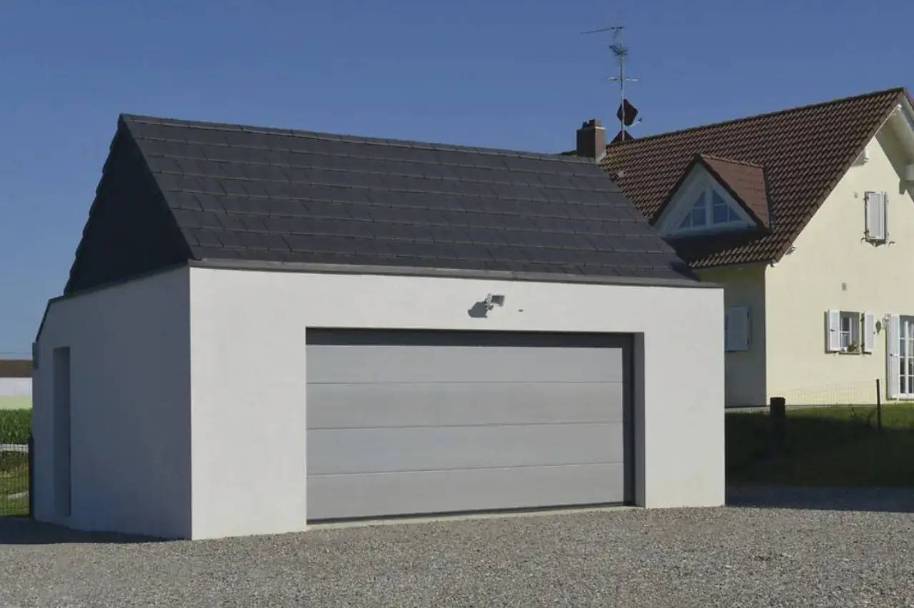 Un garage moderne en crépi blanc avec un toit en ardoise, situé à côté d'une maison.